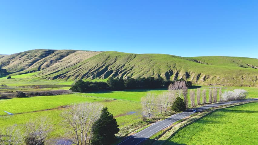 Aerial view of a winding road through lush green hills under clear blue skies in Akaroa, New Zealand
