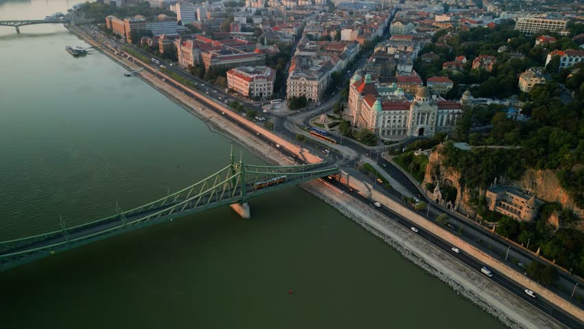Drone flight over downtown Budapest with busy bridge and flowing river in daylight, golden glow of light