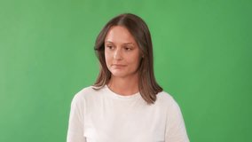 A woman with long brown hair wearing a white t-shirt stands in front of a green screen, looking slightly serious or contemplative. - Powered by Shutterstock - Get 15% off with code: PIKWIZARD15
