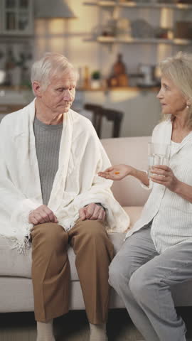 Careful wife giving pill to aged husband for curing headache and hypertension. Medicine for illness of old age, elderly man taking tablet in season of respiratory disease, temperature and fever