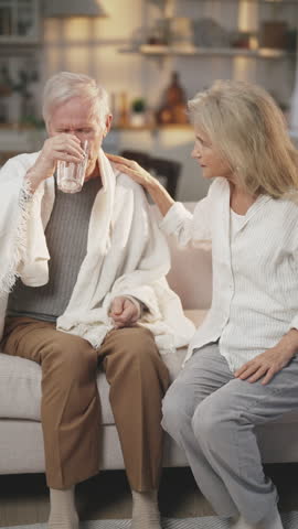 Careful wife giving pill to aged husband for curing headache and hypertension. Medicine for illness of old age, elderly man taking tablet in season of respiratory disease, temperature and fever