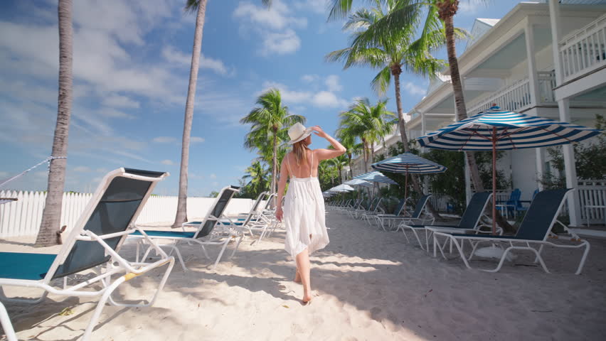 A woman strolls gracefully through the stunning scenery of a luxurious Key West hotel, capturing the breathtaking beauty around her in slow motion, all while enjoying her leisurely day to the fullest