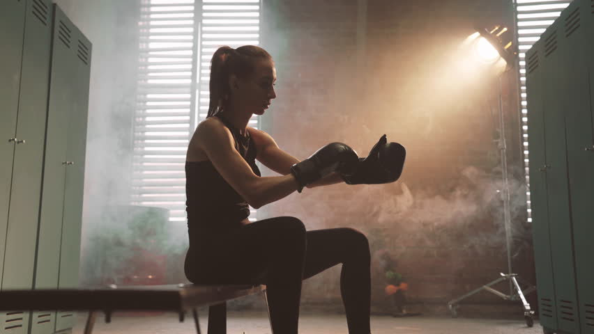 Woman putting boxing gloves in changing room before workout, sport activity. Femininity and masculinity, martial arts for women for self-defense and training endurance of body, athletic female person