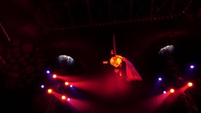 A flexible aerial gymnast performs tricks on fabric high under the dome of the circus under the light of colorful spotlights and smoke. A circus show. An aerial acrobat. - Powered by Shutterstock - Get 15% off with code: PIKWIZARD15
