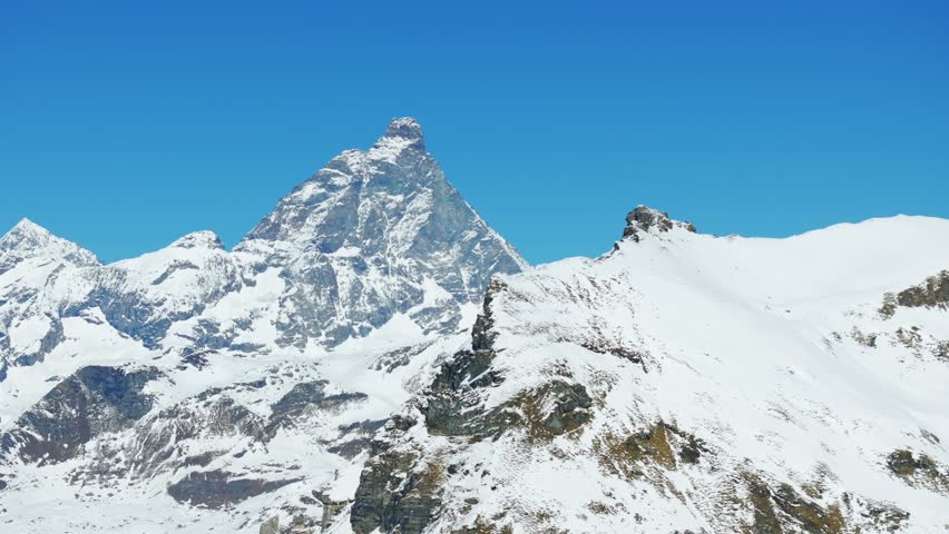 Iconic Matterhorn mountain, Cervino mount peak covered in snow against vivid blue sky, Alpine majesty, Alps. Aerial drone, low-angle pov