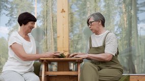 Two elderly half asian sisters sitting on suburb house terrace and talking and using fortune telling metaphorical cards and drinking coffee or tea - Powered by Shutterstock - Get 15% off with code: PIKWIZARD15