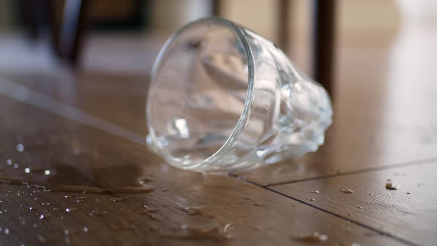 A Broken Glass Cup Has Fallen on the Wooden Floor, Creating a Mess