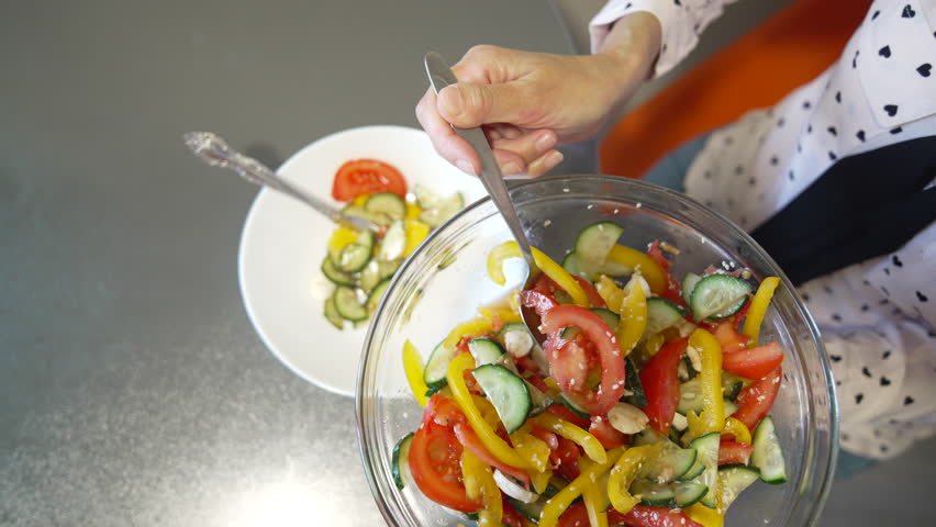 Salad Cucumbers Tomatoes Woman portions fresh salad with fork in indoor kitchen setting