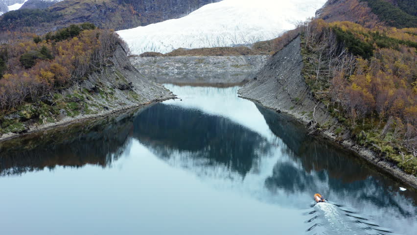 Curved river bends through lush valley with forest and hills in remote Patagonia region as speedboat enters narrows below glacier