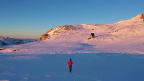 Drone Following Hiker Toward Cozy Mountain Shelter at Sunset in Serene Winter Landscape - Powered by Shutterstock - Get 15% off with code: PIKWIZARD15