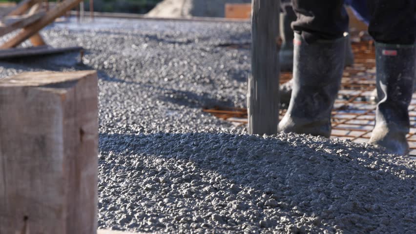 Construction workers with concrete boom pump crane at construction site pouring concrete and leveling fresh concrete floor with a wooden tool building a new house, slow motion