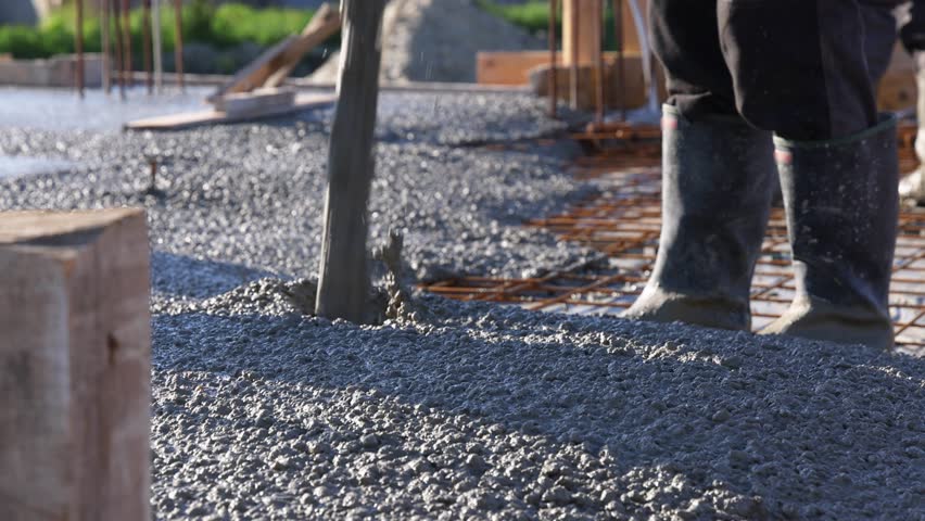 Construction workers with concrete boom pump crane at construction site pouring concrete and leveling fresh concrete floor with a wooden tool building a new house, slow motion