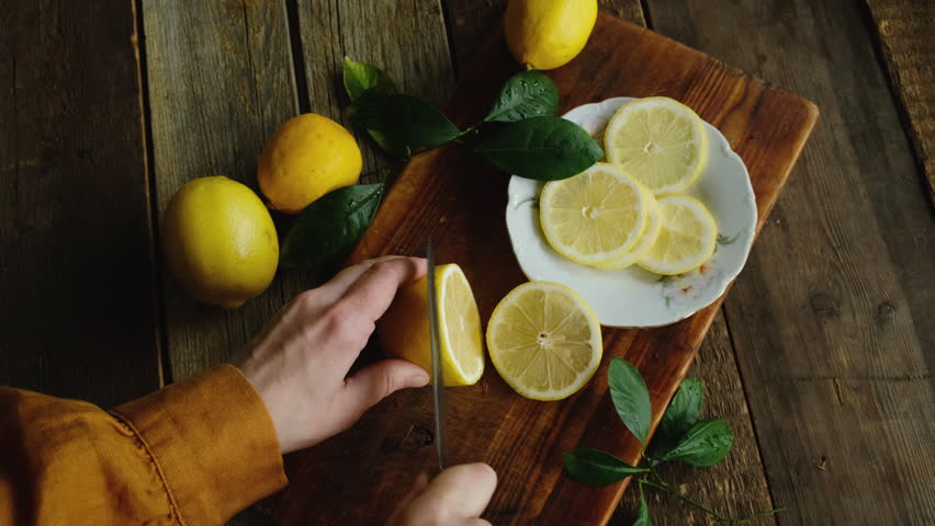 Summer food. Lemon slicing. Female hands cutting fresh lemons into slices. Top view.