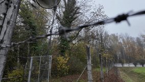 A close-up of an old floodlight attached to a barbed wire fence post, captured on a misty day with dense foliage and a locked gate in the blurred background, evoking a somber atmosphere. - Powered by Shutterstock - Get 15% off with code: PIKWIZARD15