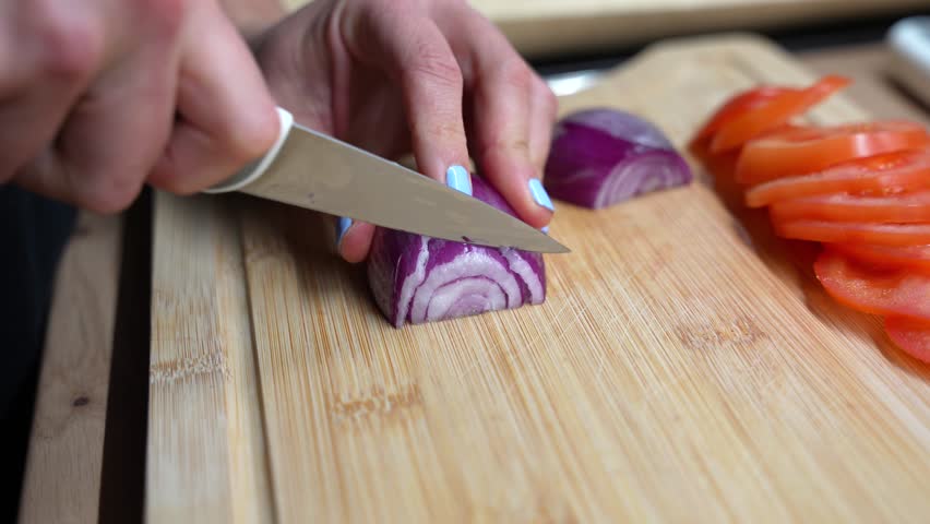Close-up of woman cutting red onions in kitchen. Slicing raw ingredients