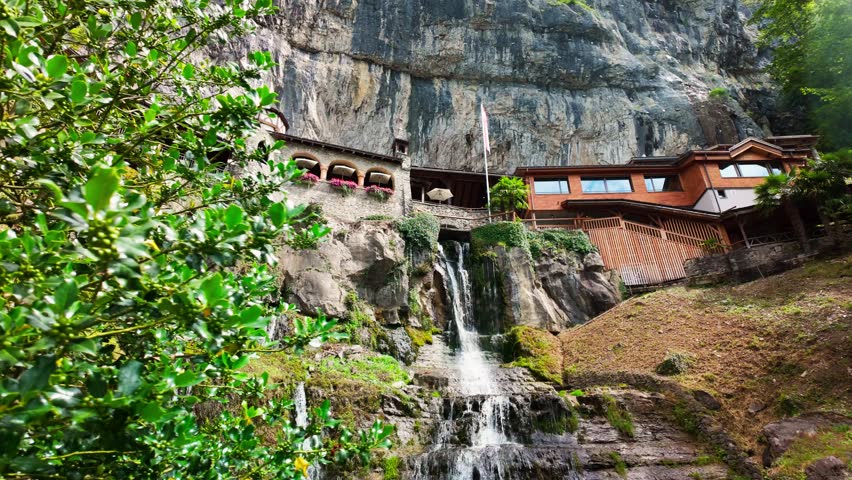 Scenic view of St. Beatus Caves entrance built into a cliffside with cascading waterfalls near Interlaken, Switzerland.