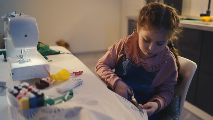 Little girl cutting fabric and fitting it on doll, developing sewing hobby