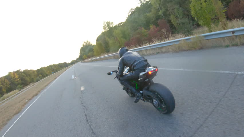 Camera moving around of biker riding on modern sport motorbike at highway. Motorcyclist racing his motorcycle on country road at sunset. Man driving bike during trip. Concept of freedom and adventure