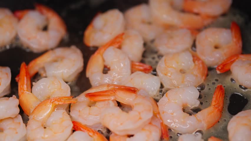 Fresh shrimp sauteing in hot pan with steam and golden crust forming during frying saute process with steam