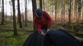 Camping, tourism and travel concept. Man setting up tent outdoors. Hiker assembles campsite tent in the autumnal forest. Traveler installing tent in autumn woods. Outdoor weekend Activity.  - Powered by Shutterstock - Get 15% off with code: PIKWIZARD15
