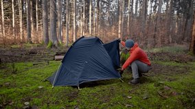 Man hiker sets up camping tent in the fall forest on backpacking expedition. Traveler setting an overnight tent in the wilderness in the fall. Theme of tourism and trekking. Outdoor weekend activity.  - Powered by Shutterstock - Get 15% off with code: PIKWIZARD15