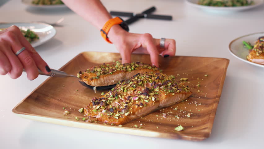 Woman serving salmon from oven to friend having lunch at table at home. Warm meal shared in cozy dining space, highlighting homemade food and togetherness