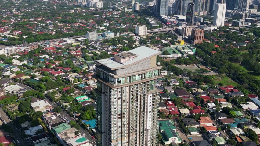 Aerial pullback of residential condominium tower, Viridian in Greenhills, surrounded by homes and cityscape in San Juan City, Philippines.