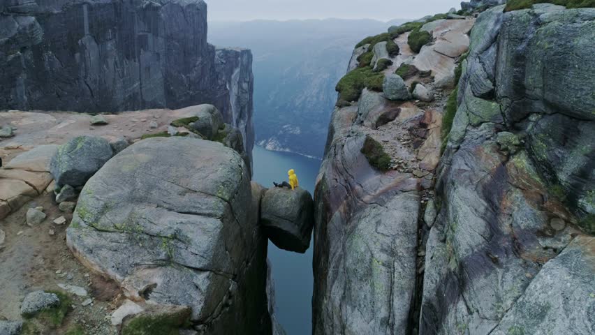 Solo traveler in yellow jacket balanced on boulder wedged between high cliffs