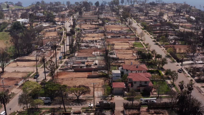 Low aerial shot tilting up to reveal fire debris in a residential neighborhood after the Palisades Fire in Los Angeles, California. 4K