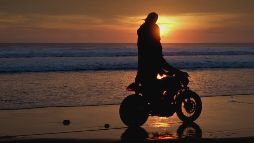 Romantic couple rides a motorcycle on a sand beach, holding red warning light. Man, woman drive stylish retro bike along ocean or sea shore, burning torch. Male, female in road trip on tropical island