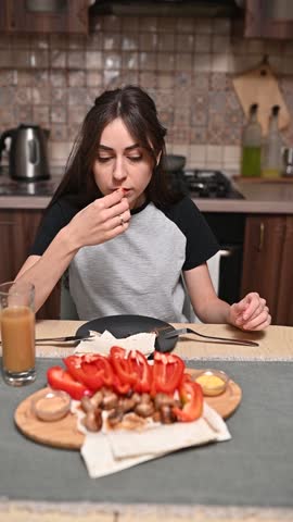 Young woman is sitting at her kitchen table, preparing a healthy healthy of vegetables, pita bread, and juice breakfast meal food