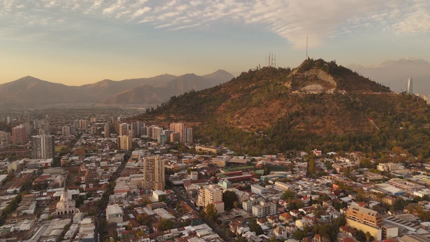 Aerial view of de Chile's cityscape and the expansive Parque Metropolitano during a vibrant sunset. Filmed in stunning 4K resolution at 60fps for smooth, detailed visuals.