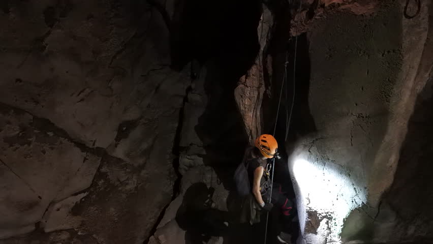A caver uses the Single Rope Technique (SRT) to descend into the dark and mysterious Anxiety State Cave in Chiang Mai, headlamp illuminating the textured rock walls.