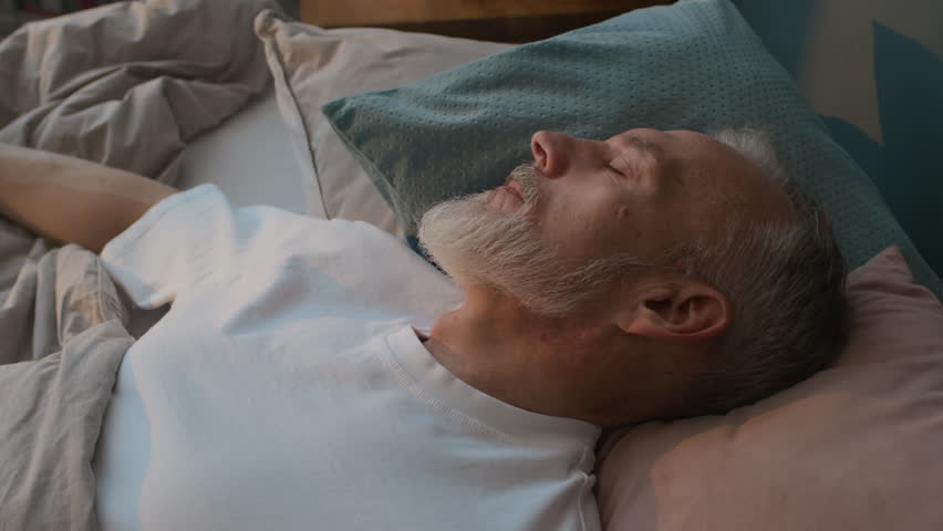 Close up view of senior man in white t-shirt sleeping in comfortable bed at home