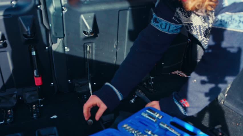 A Person is Working Inside a Pajero, Using a Ratchet Wrench to Remove Bolts Near the Rear Seat Area, With a Toolkit Placed Nearby - Close Up