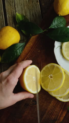 Vertical video. Summer food. Lemon slicing. Hands cutting fresh lemons into slices. Top view.