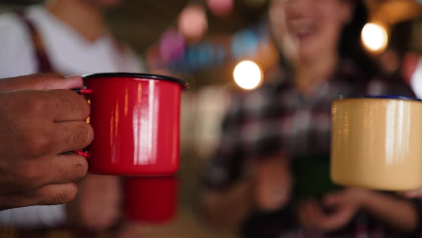 Close-Up Celebration with Steel Mugs at Brazilian June Festival Toast. Friends Raising Colorful Cups in a Festive Salute at Festa Junina Gathering