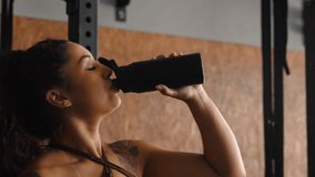 Young African American female fitness enthusiast with natural curly hair drinking from black insulated water bottle during workout break in contemporary facility - Powered by Shutterstock - Get 15% off with code: PIKWIZARD15