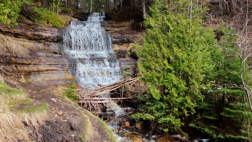 Alger Falls cascading down layered rock near Pictured Rocks National Lakeshore in Michigan with roadside view and natural surroundings.