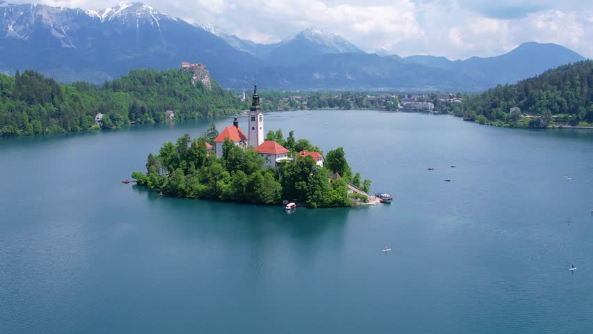 Aerial view of Church of the Assumption of Mary in the center of the lake Bled. Flying around small island on Bled Lake in Slovenia, warm summer day sun