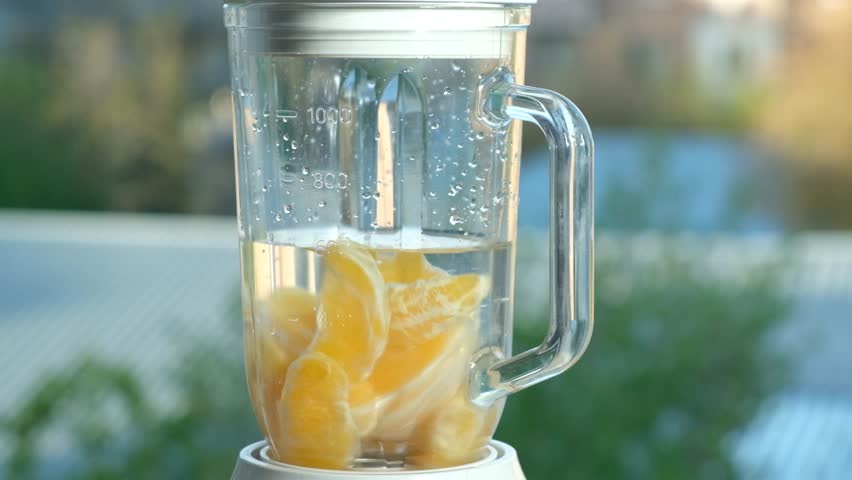 Blender turned on and mixing fresh oranges to make juice. Slicing and blending citrus fruits for a natural cocktail. Preparing an organic fruit drink. Healthy lifestyle and clean nutrition