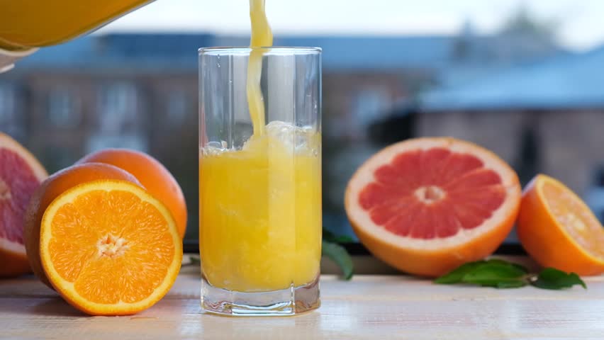 Slow-motion pour of citrus cocktail with pulp into a glass with ice cubes. Refreshing juice made from orange and grapefruit. Chilled fruit drink for a healthy and energizing refreshment.