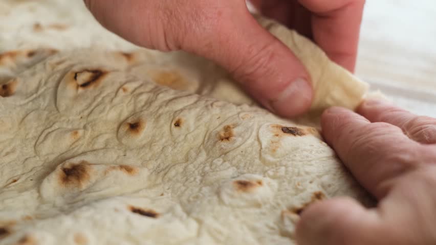 Male hands tear fresh traditional lavash bread, showing its many thin layers. Soft unleavened flatbread commonly used in Eastern cuisine. Armenian lavash as a part of national food culture