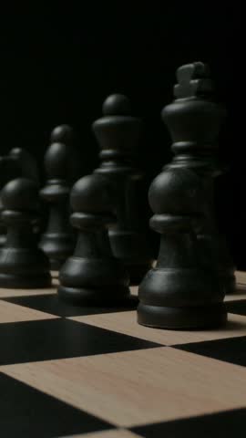 Black plastic chess pieces on black and white checkerboard. Wide macro dolly in. Ready for epic chess game concept. Vertical shot.