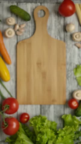 Slow motion shot of sliced carrot falling on wooden chopping board and spreading over kitchen table with mushrooms and vegetables Vertical shot.