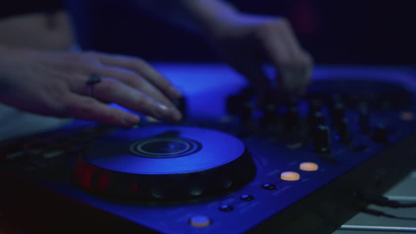 DJ mixes music using an audio mixer and turntables on stage. Knobs in hand, slide scratch