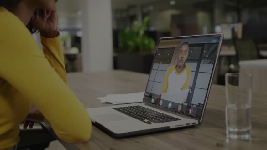 female colleagues holding remote technology meeting at office desk, showing floating code overlay. Collaboration, digital, modern, workspace, communication, networking, productivity
