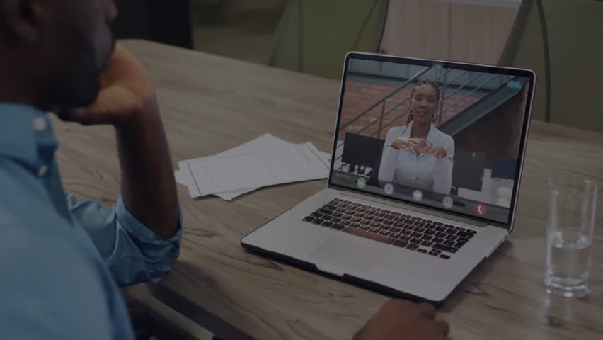 man wearing blue shirt joining business call on laptop with papers, water glass, binary code. Corporate, communication, workspace, professionalism, technology, collaboration, modern - Powered by Shutterstock - Get 15% off with code: PIKWIZARD15