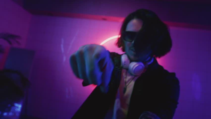 Man dancing at a techno rave party. Male mixing tracks by DJ controller at pink blue disco club