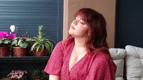 Beautiful young curvy woman with long auburn hair and red dress, sitting on a balcony with potted plants, breathing fresh air and enjoying a moment of relaxation - Powered by Shutterstock - Get 15% off with code: PIKWIZARD15